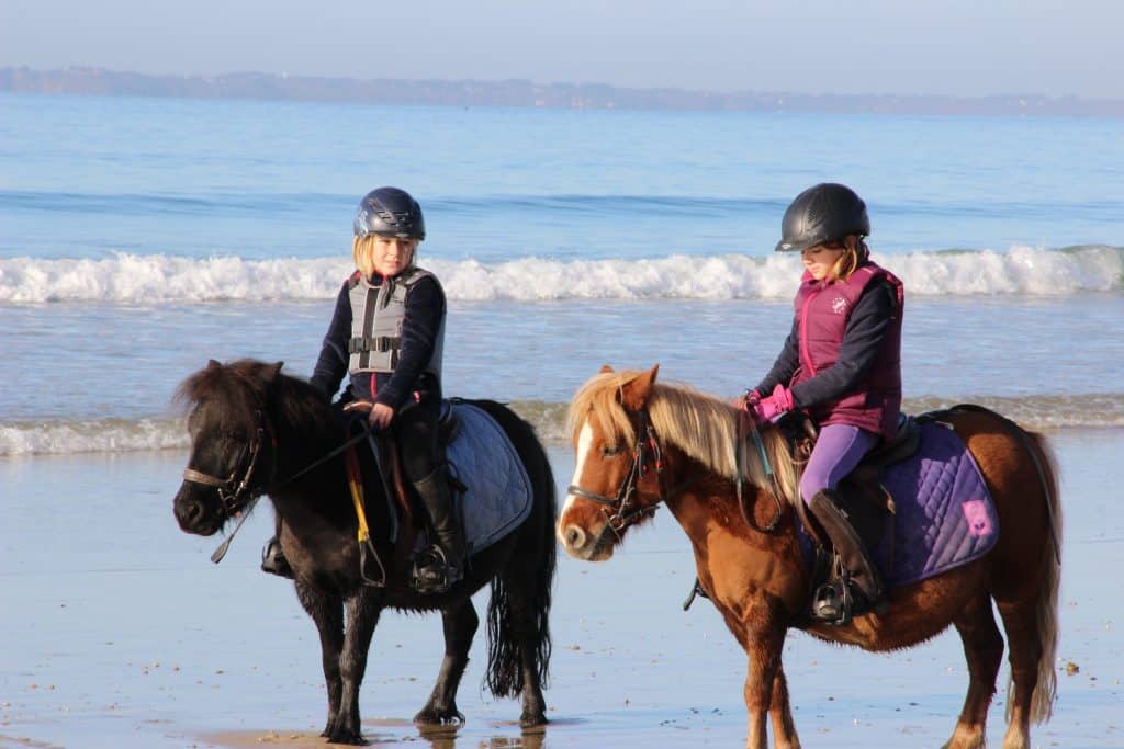 Enfants à cheval sur la plage, mer et vagues.