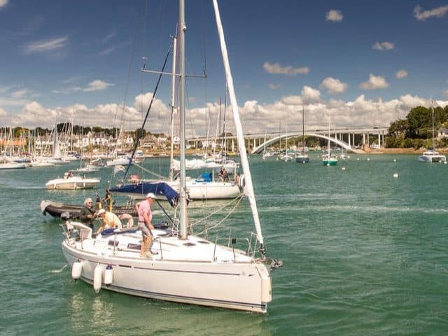 Voilier naviguant dans un port ensoleillé de Bretagne.