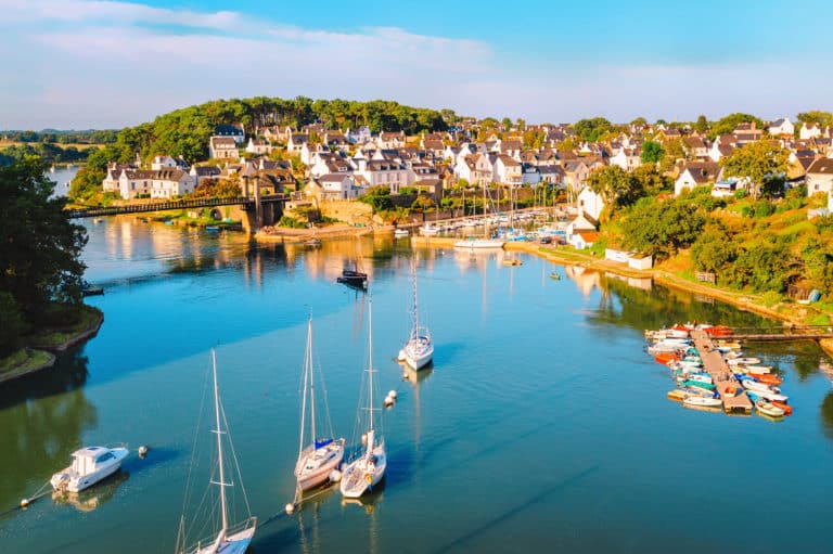 Port pittoresque avec voiliers, village en arrière-plan.